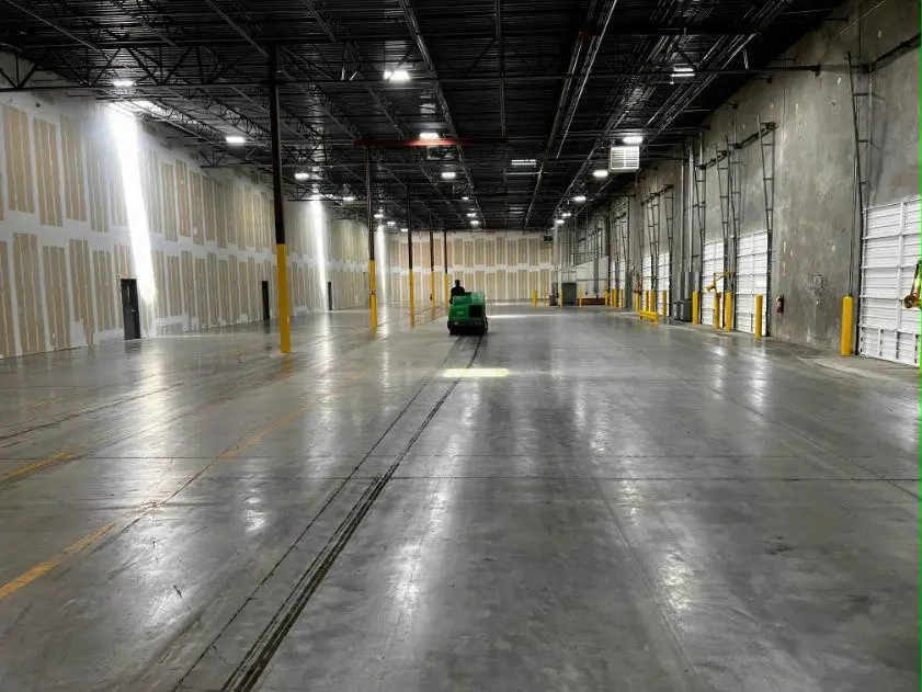 Ride-on floor scrubber in large industrial warehouse post-construction cleanup Charlotte NC